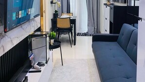 Una sala de estar moderna con un televisor de pantalla plana, un comedor con mesa y sillas, un sofá e iluminación empotrada en el techo.