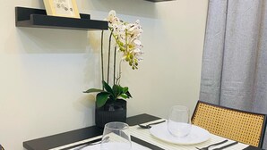 Una mesa de comedor con dos platos blancos, cubiertos y una copa. Hay dos sillas, un camino de mesa negro y una orquídea en maceta en la pared.