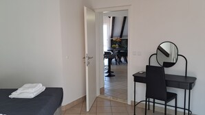 Habitación de hotel con cama, escritorio con silla, espejo y vista al área de comedor.