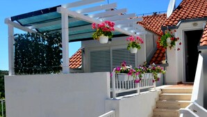 Un espacio al aire libre cubierto con barandilla blanca, escalones que llevan a una puerta y cestas de flores colgantes.