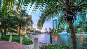 A waterfront promenade with palm trees, a canal, and modern buildings in the background. - Coastal Luxury - 5 min to beach (Fort Lauderdale)