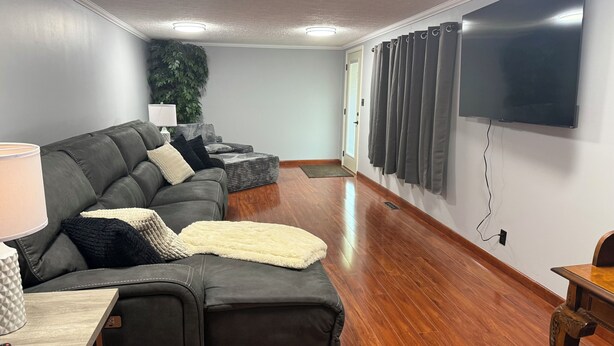 A modern living room with a sectional sofa, a flat-screen TV, and a wooden floor.