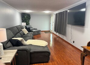 A modern living room with a sectional sofa, a flat-screen TV, and a wooden floor. - The Lazy Gray – Peaceful Stay Near Jackson Lake - Pet Friendly (Oak Hill)