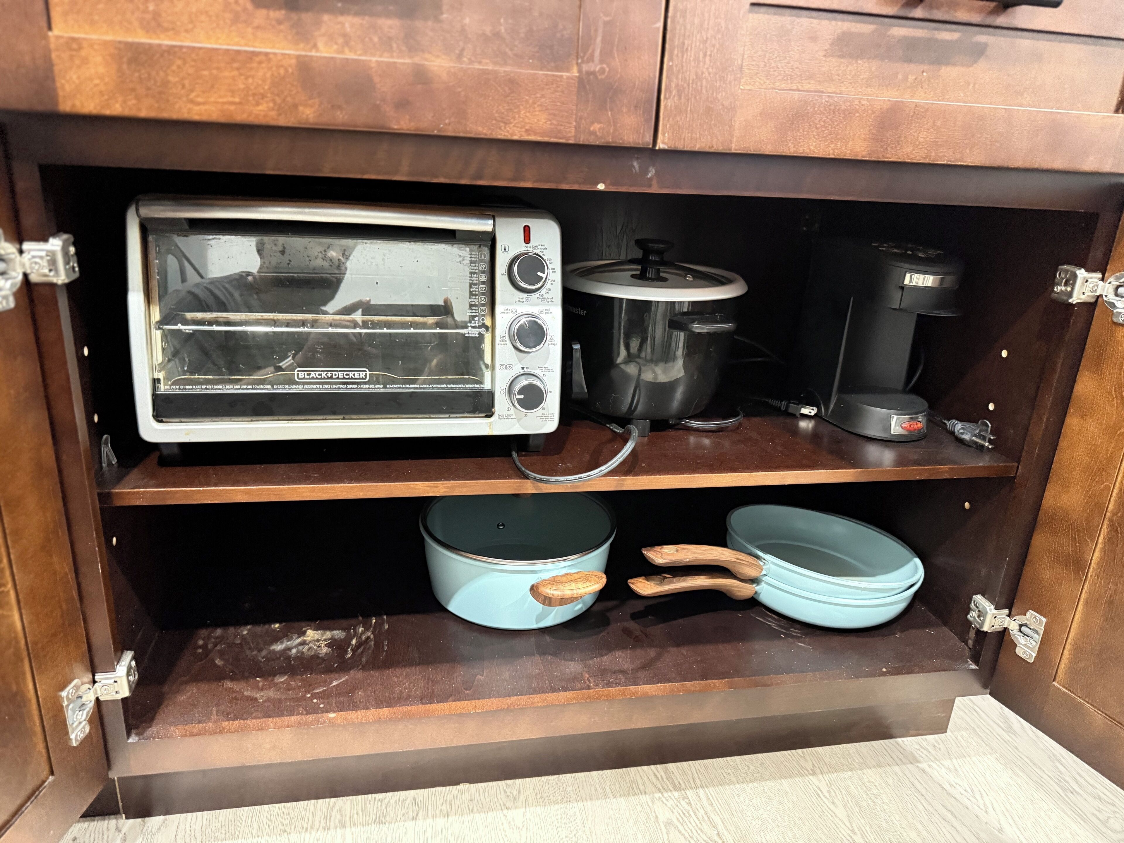 A kitchen with a toaster oven, a coffee maker, and two blue pots on a wooden shelf.