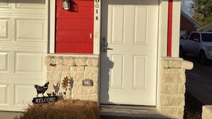 Una casa roja con puerta de garaje blanca, un letrero de bienvenida con gallinas y un buzón.