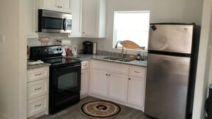Una cocina con armarios blancos, un refrigerador de acero inoxidable, una estufa negra y un microondas.