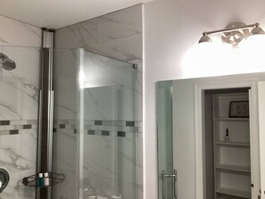 Bathroom features a glass-enclosed shower with clear glass door and vertical panel, and a separate area with a white shelf unit.