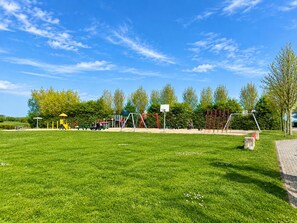 Een speeltuin met diverse speeltoestellen, een basketbalveld en een verhard wandelpad.