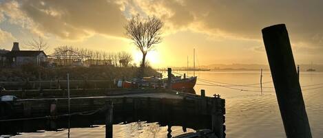 Un muelle con barcos amarrados, una masa de agua tranquila y una puesta de sol al fondo.
