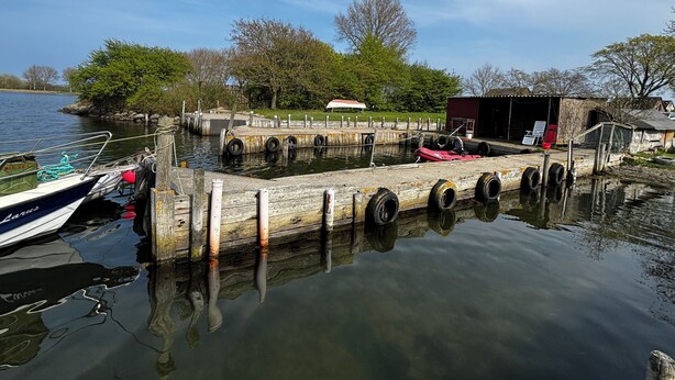 Een steiger met een boot, een rode kajak en een klein tuinhuis aan het water.