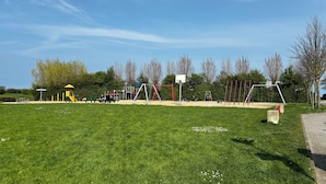 Een speeltuin met diverse speeltoestellen, een basketbalveld en een picknickplaats.