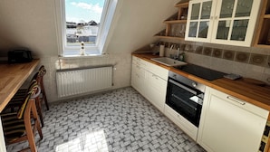 Een keuken met een raam, witte kasten, een houten aanrechtblad en een betegelde vloer.