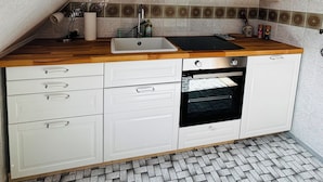 Een keuken met een houten aanrechtblad, witte kasten, een inbouwoven en een betegelde spatwand.