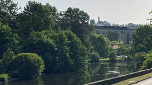 Ein Fluss mit einer Brücke im Hintergrund, umgeben von Bäumen und Grün.