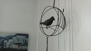 Ein an der Wand befestigter Vogelkäfig mit einem Vogel darin, ein gerahmtes Foto von Gebäuden und eine weiße Wand.