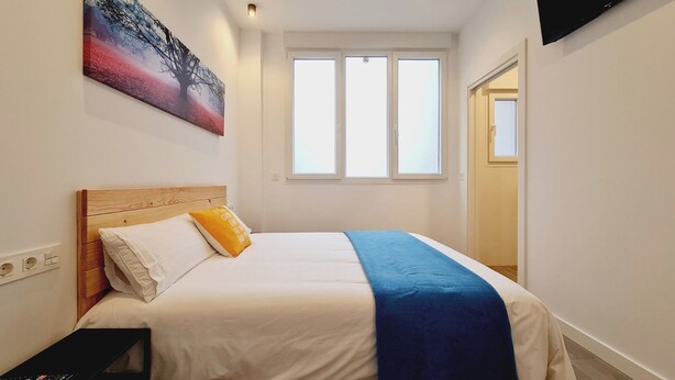 A hotel room with a bed, a TV, a window, and a painting on the wall. - Bilbao ROOMS Etxebarria (Bilbao)