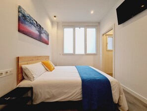 A hotel room with a bed, a TV, a window, and a painting on the wall. - Bilbao ROOMS Etxebarria (Bilbao)