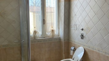 Un baño con ducha, dos inodoros y una ventana con cortinas.
