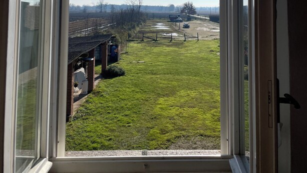 A view through a window with a hanging light fixture, a grassy area, and a distant road. - BeB Cascina Mentirone (Rosate)