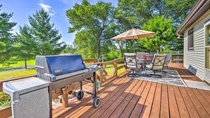 A wooden deck with a grill, outdoor furniture, and a view of a green landscape.