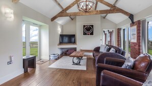 Un salón amplio con techo de madera, televisor grande, sofás de cuero y chimenea.