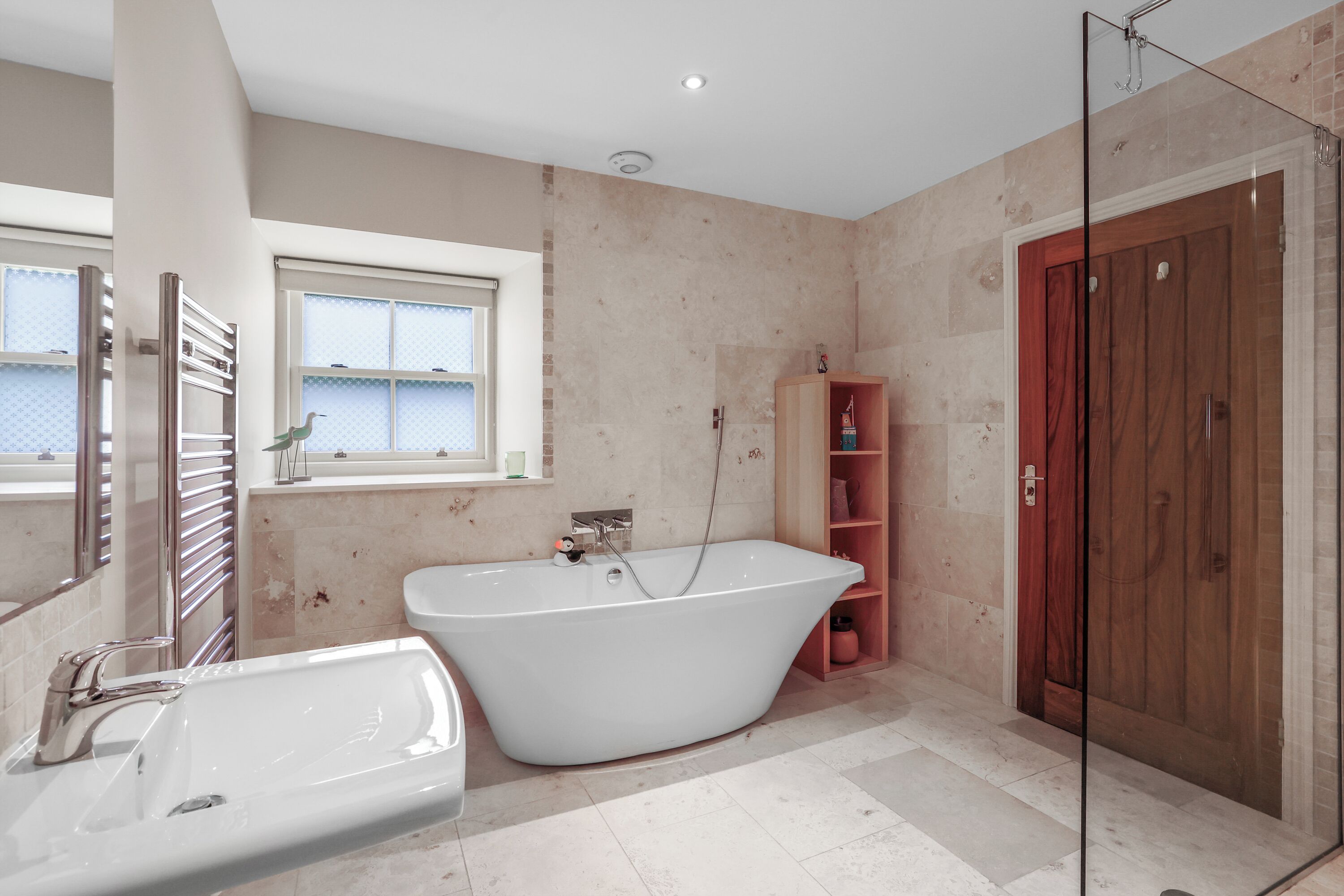 Ein modernes Badezimmer mit freistehender Badewanne, einer gläsernen Dusche und einem Holzkosmetikschrank.