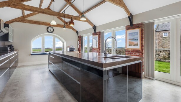 Una cocina moderna con una isla grande, vigas de madera a la vista, ventanas amplias y vistas al campo.