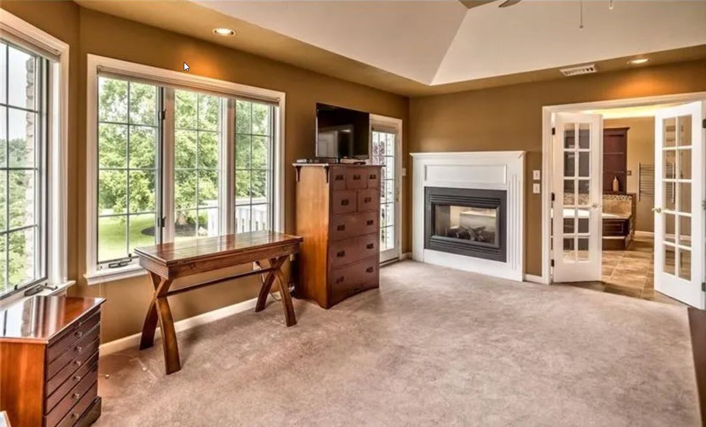 A spacious room with a large window, a fireplace, and a wooden desk.