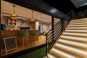 A modern interior with a wooden bar area, green chairs, and a staircase with a metal railing.