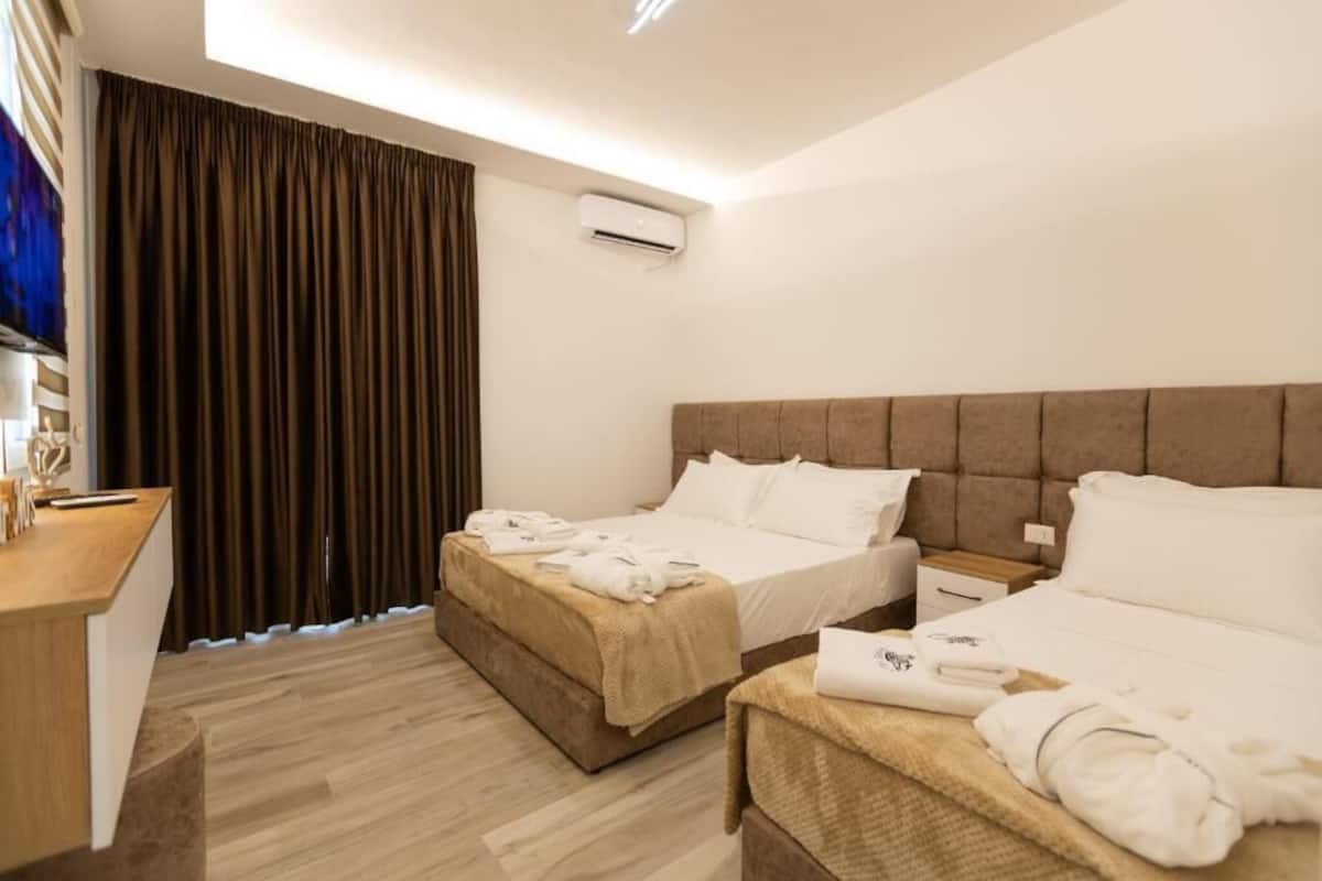 Hotellihuone, jossa on kaksi sänkyä, työpöytä ja suuri ikkuna, jossa on verhot.