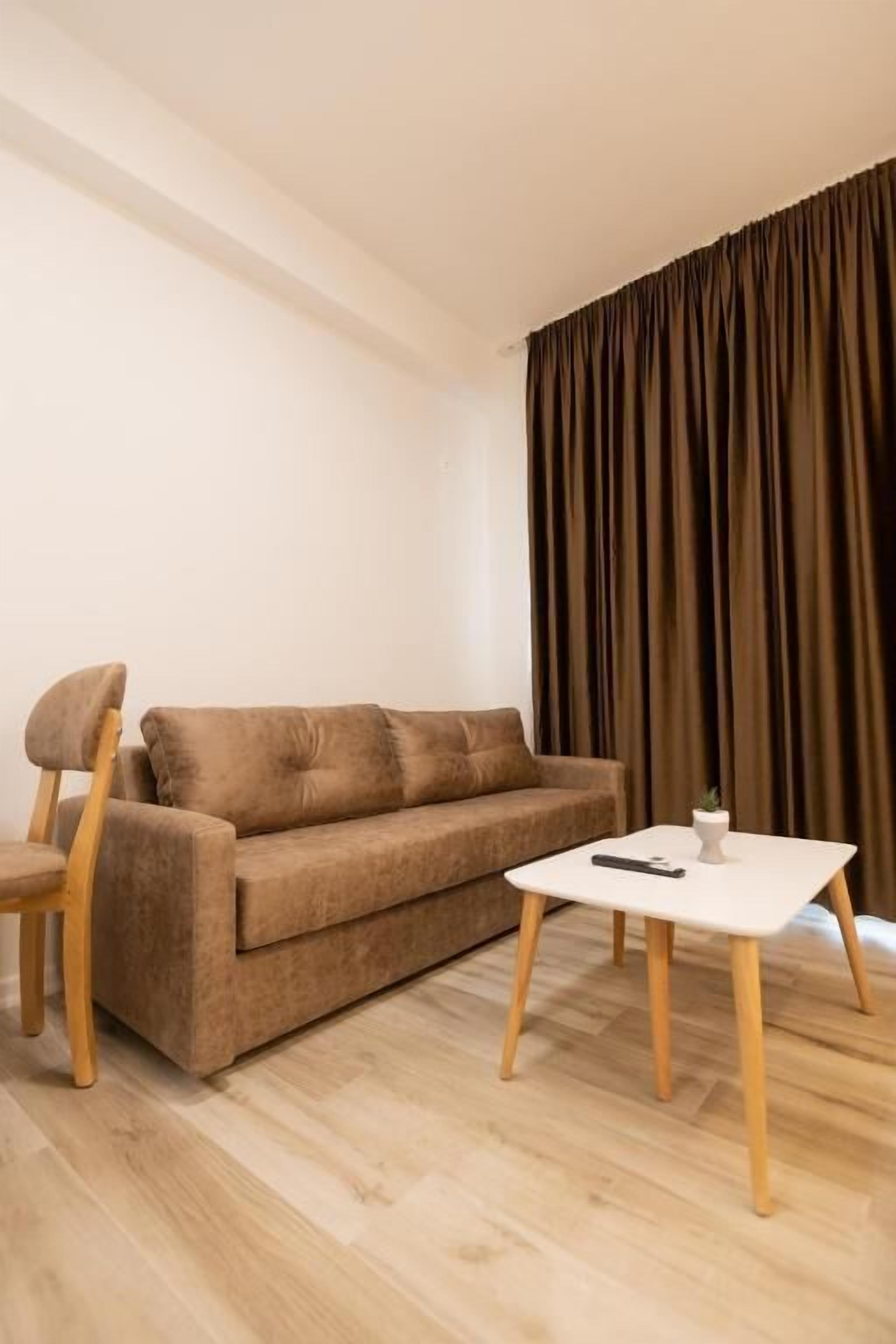 A living room with a brown sofa, a wooden chair, a white coffee table, and a remote control on it.