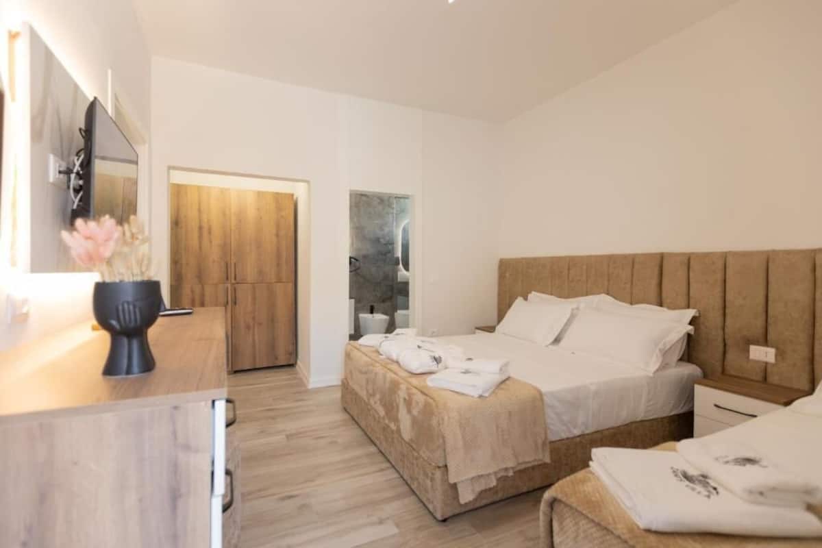 Moderni hotellihuone, jossa on puinen sänky, yöpöytä ja suuri peili.