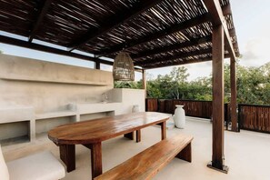 Une terrasse extérieure avec une table et des bancs en bois, un luminaire suspendu et un mur en béton.