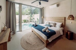 A bedroom with a bed, a wooden headboard, a bedside table, a round rug, and a view of an outdoor area with a pool. - Casa Zara Tulum Jungle Villa Sleeps 8 Beach Club (Tulum)