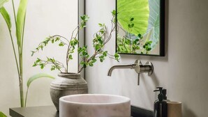 Une salle de bain moderne avec un lavabo rond, un miroir, un robinet, un distributeur de savon et une serviette.