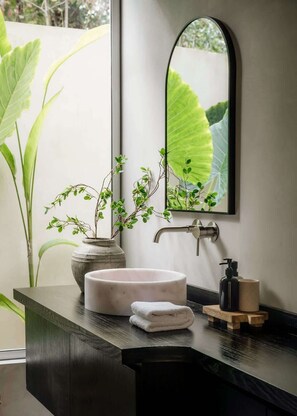 Un baño moderno con un lavabo redondo, un espejo, un grifo, un dispensador de jabón y una toalla.