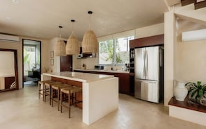 A modern kitchen with a central island, pendant lights, and a refrigerator.