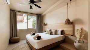 Une chambre à coucher avec un lit, un ventilateur de plafond, une fenêtre avec des rideaux, une lampe de chevet et un vase contenant des plantes séchées.