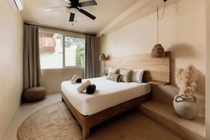 A bedroom with a bed, a ceiling fan, a window with curtains, a bedside lamp, and a vase with dried plants.
