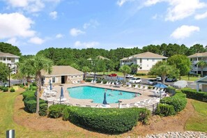 A swimming pool with lounge chairs and umbrellas, surrounded by well-maintained landscaping and residential buildings. - Stylish Barefoot Golf Condo with Pool Access (North Myrtle Beach)