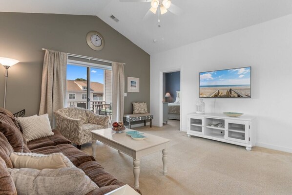A living room with a sofa, a coffee table, a TV, and a view of the outside.