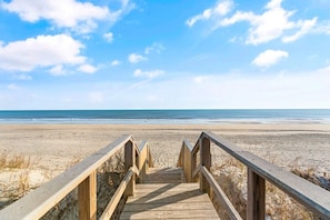 Une promenade en bois qui mène à une plage, avec un ciel dégagé.