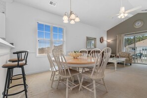 A dining area with a round table, white chairs, a bar stool, and a ceiling fan.