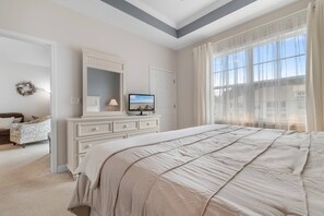 A bedroom with a large bed, a dresser, a television, and a window with curtains.