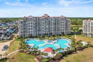 A large hotel with multiple floors, a central swimming pool, and surrounding greenery.