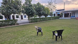 A grassy outdoor area with two black plastic chairs. - Govind Resort (Mathura)