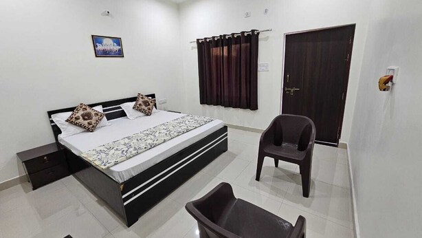 A bedroom with a bed, a chair, a small table, a wardrobe, and a picture on the wall. - Govind Resort (Mathura)