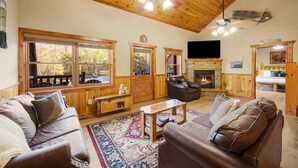 Ein gemütliches Wohnzimmer mit Kamin, Ledersofas, einer Holzbalkendecke und großen Fenstern.