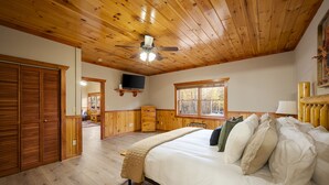 Ein Schlafzimmer mit Holzboden, einem Bett mit vielen Kissen, einer Kommode und einem an der Wand befestigten Fernseher.