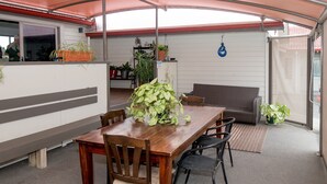 Un espacio de comedor techado con mesa y sillas de madera, un sofá y plantas en macetas.